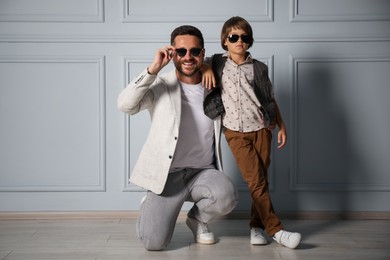 Photo of Father and son in stylish outfits posing near light wall