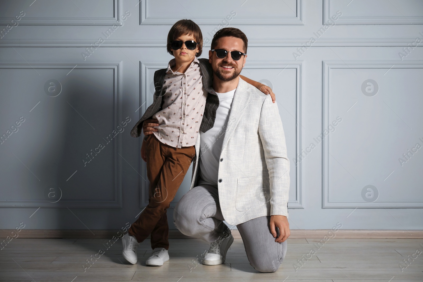 Father and son in stylish outfits posing near light wall Photo of Father and son in stylish outfits posing near light wall