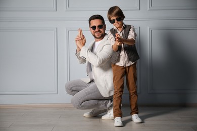Photo of Father and son in stylish outfits posing near light wall