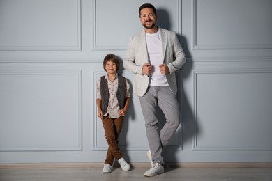 Photo of Father and son in stylish outfits posing near light wall