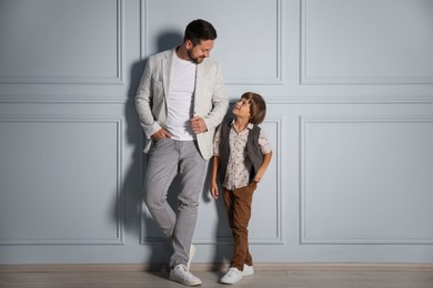 Photo of Father and son in stylish outfits posing near light wall