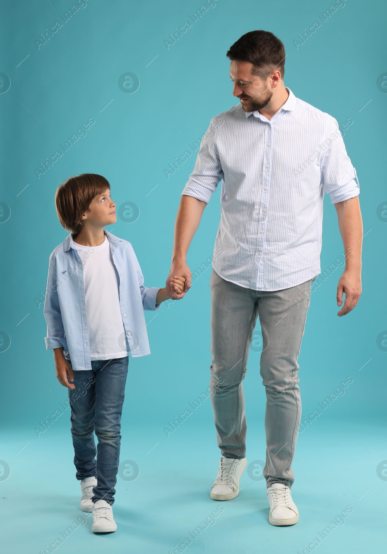 Photo of Father and son holding hands while walking on light blue background