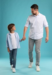 Photo of Father and son holding hands while walking on light blue background