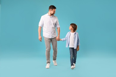 Photo of Father and son holding hands while walking on light blue background
