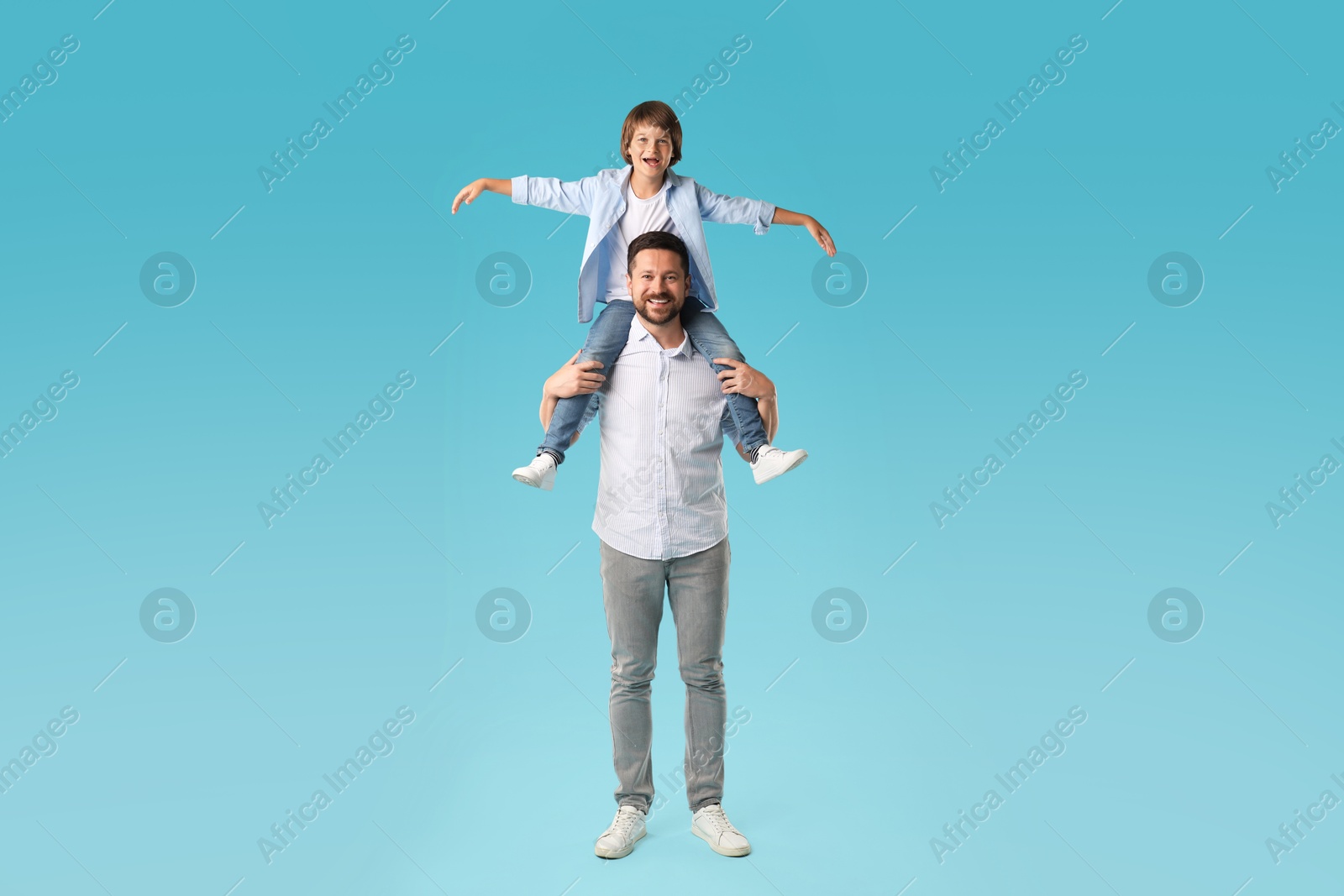 Father carrying his son on shoulders against light blue background Photo of Father carrying his son on shoulders against light blue background