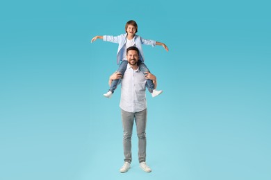 Photo of Father carrying his son on shoulders against light blue background
