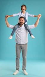 Photo of Father carrying his son on shoulders against light blue background
