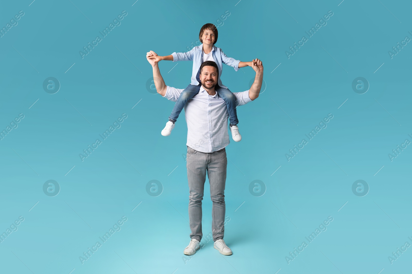 Father carrying his son on shoulders against light blue background Photo of Father carrying his son on shoulders against light blue background