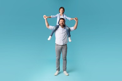 Photo of Father carrying his son on shoulders against light blue background