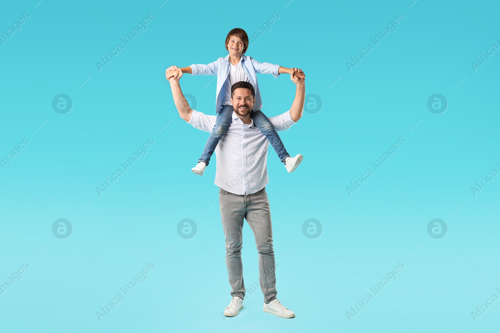 Father carrying his son on shoulders against light blue background Photo of Father carrying his son on shoulders against light blue background