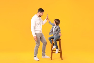 Photo of Father and son giving high five on yellow background