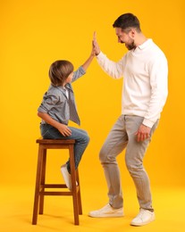 Photo of Father and son giving high five on yellow background