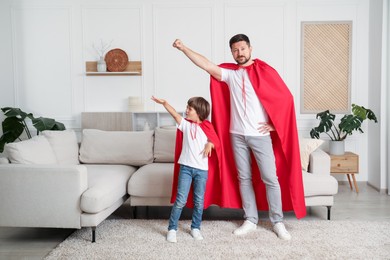 Photo of Father and son in red capes playing superheros at home