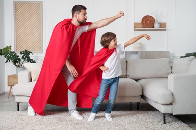 Photo of Father and son in red capes playing superheros at home