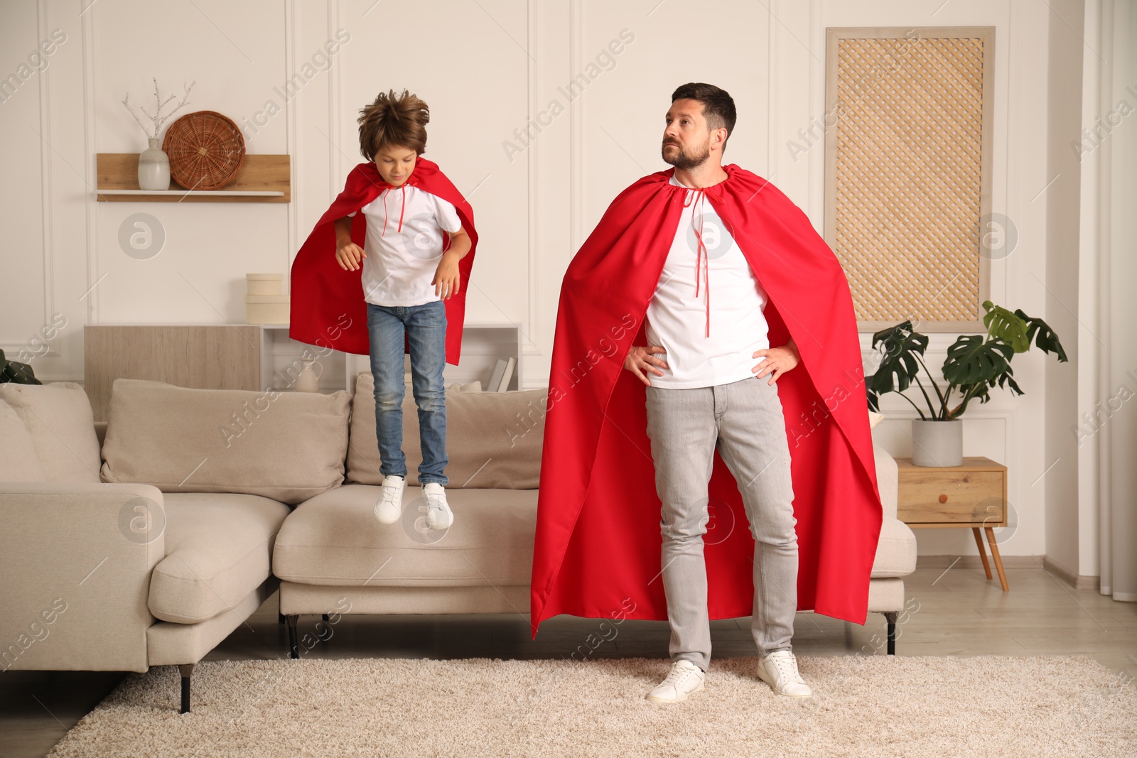 Father and son in red capes playing superheros at home Photo of Father and son in red capes playing superheros at home
