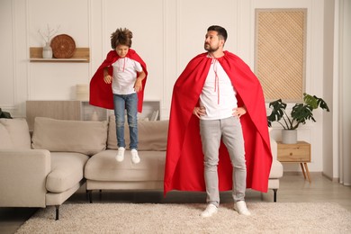 Photo of Father and son in red capes playing superheros at home