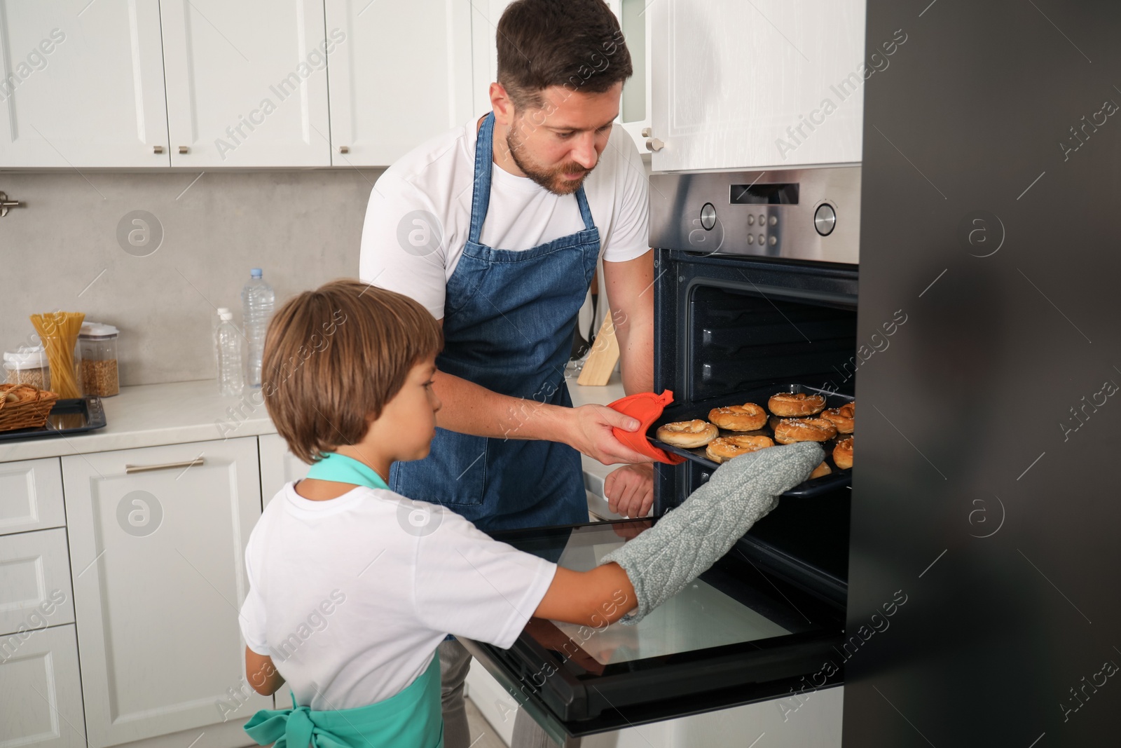 Father and son taking baking tray with pastries out of oven at home Photo of Father and son taking baking tray with pastries out of oven at home