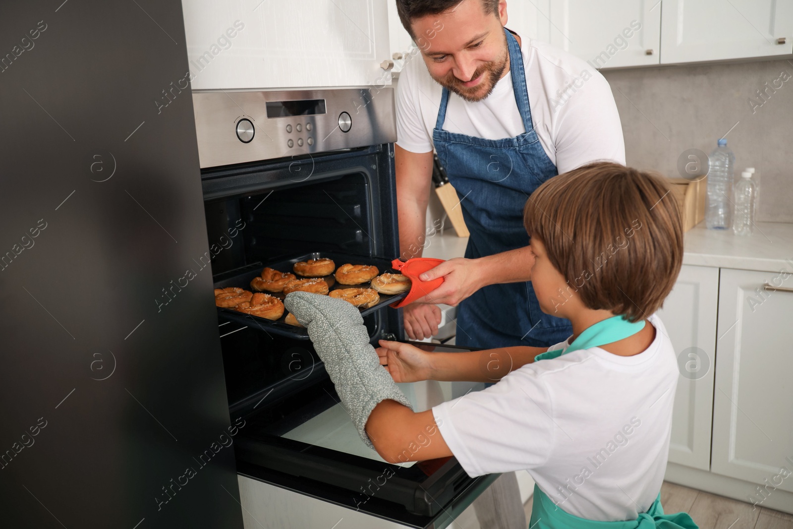 Father and son taking baking tray with pastries out of oven at home Photo of Father and son taking baking tray with pastries out of oven at home