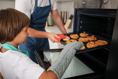 Photo of Father and son taking baking tray with pastries out of oven at home, closeup