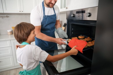 Photo of Father and son taking baking tray with pastries out of oven at home, closeup