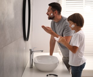 Photo of Father and son applying shaving foam on their faces in bathroom