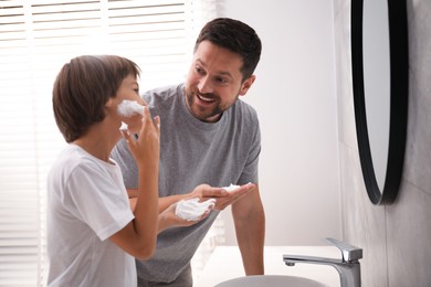 Photo of Father and son applying shaving foam on their faces in bathroom
