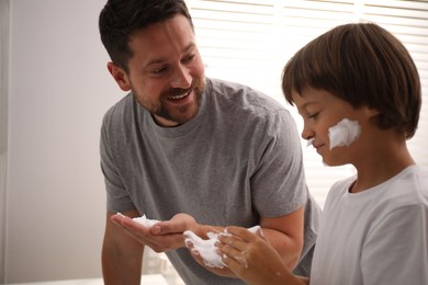 Photo of Father and son applying shaving foam on their faces in bathroom
