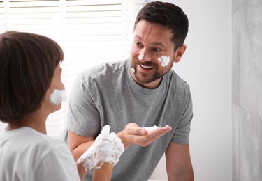 Photo of Father and son applying shaving foam on their faces in bathroom