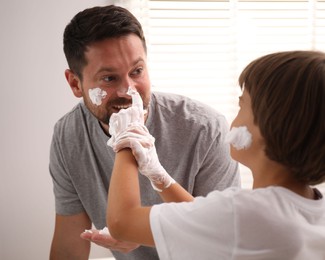 Photo of Father and son applying shaving foam on their faces in bathroom