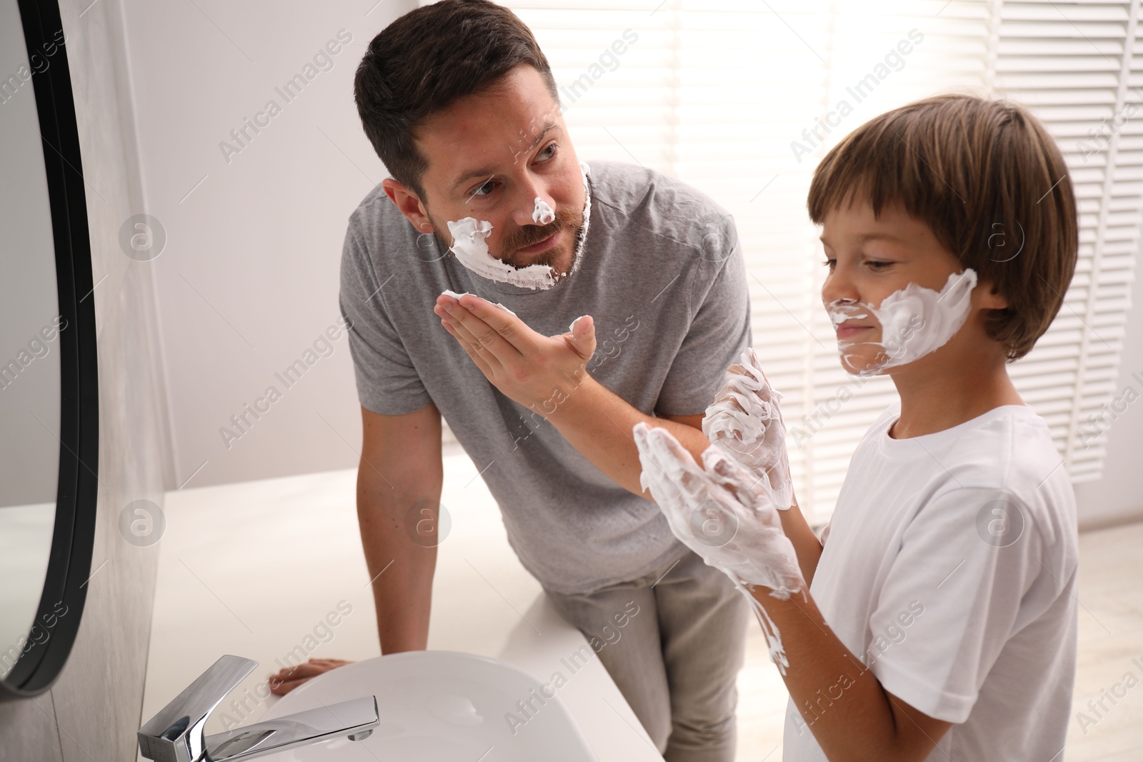 Father and son applying shaving foam on their faces in bathroom Photo of Father and son applying shaving foam on their faces in bathroom