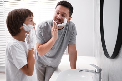 Photo of Father and son applying shaving foam on their faces in bathroom