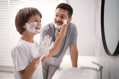 Photo of Father and son applying shaving foam on their faces in bathroom