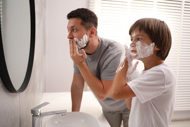 Photo of Father and son applying shaving foam on their faces in bathroom