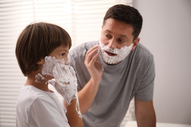 Photo of Father and son with shaving foam on their faces in bathroom