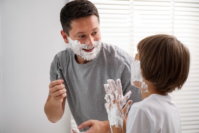 Photo of Father and son with shaving foam on their faces in bathroom