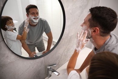 Photo of Father and son with shaving foam on their faces in bathroom