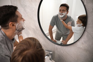 Photo of Father and son with shaving foam on their faces in bathroom