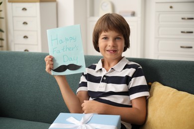 Photo of Little boy with Happy Father's Day card and gift on sofa at home