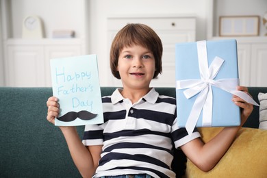 Photo of Little boy with Happy Father's Day card and gift on sofa at home