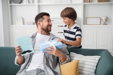 Photo of Happy Father's Day. Son giving his dad card and present at home