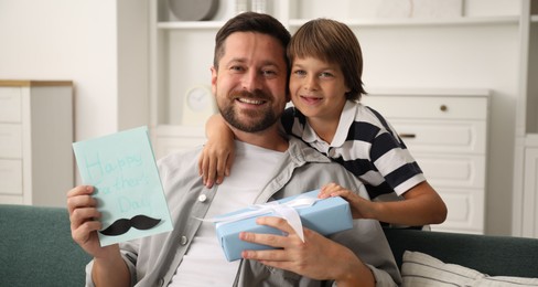 Photo of Happy Father's Day. Son giving his dad card and present at home
