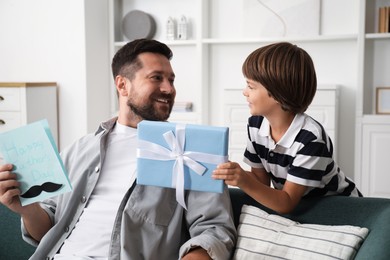 Photo of Happy Father's Day. Son giving his dad card and present at home