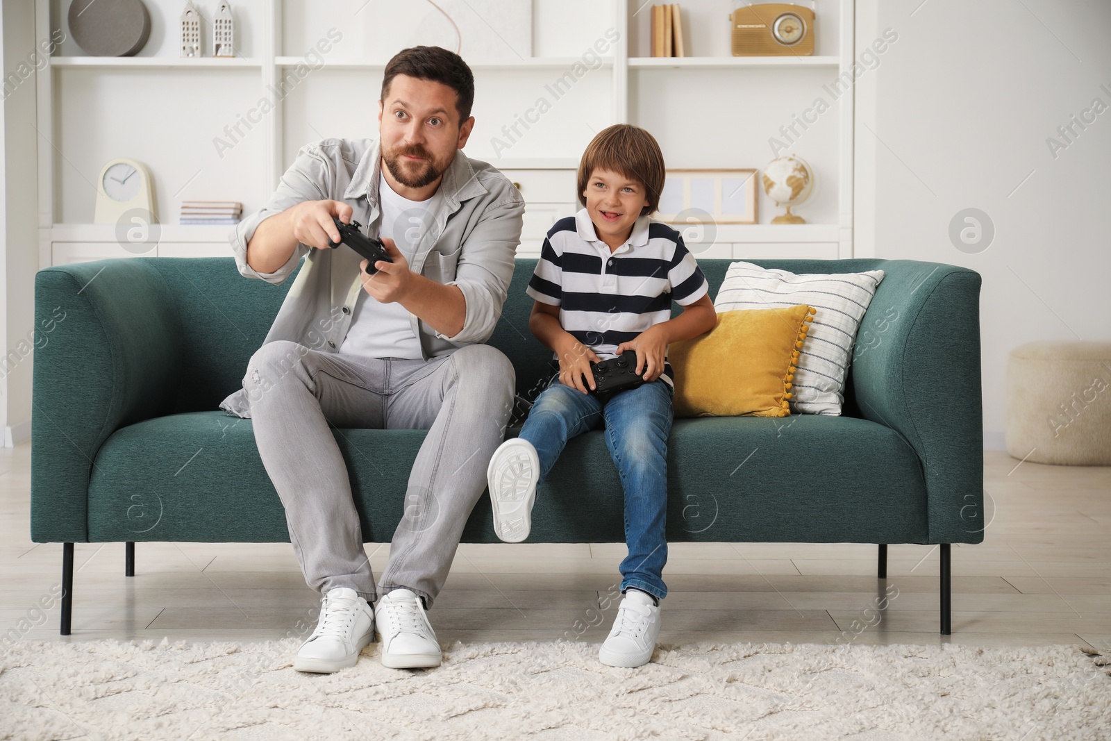 Photo of Father and son with controllers playing videogame on sofa at home