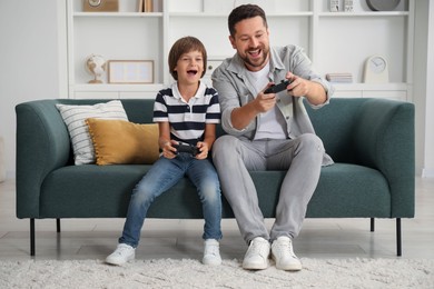 Photo of Father and son with controllers playing videogame on sofa at home