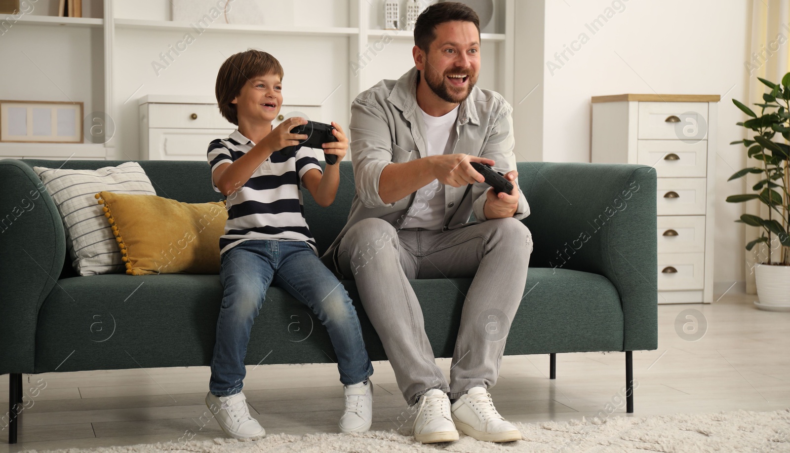 Father and son with controllers playing videogame on sofa at home Photo of Father and son with controllers playing videogame on sofa at home