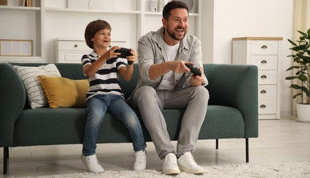 Photo of Father and son with controllers playing videogame on sofa at home