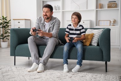 Photo of Father and son with controllers playing videogame on sofa at home