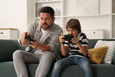 Photo of Father and son with controllers playing videogame on sofa at home