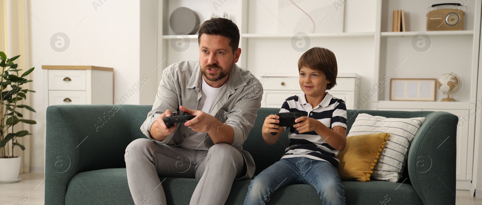 Father and son with controllers playing videogame on sofa at home Photo of Father and son with controllers playing videogame on sofa at home