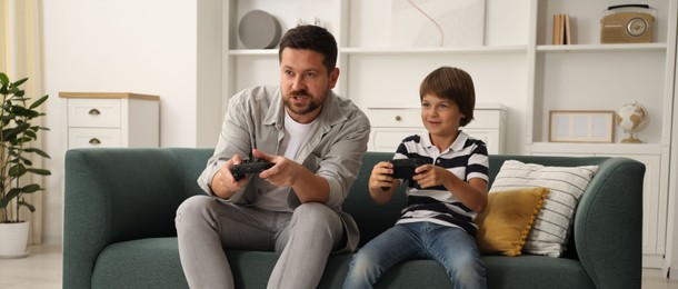 Photo of Father and son with controllers playing videogame on sofa at home